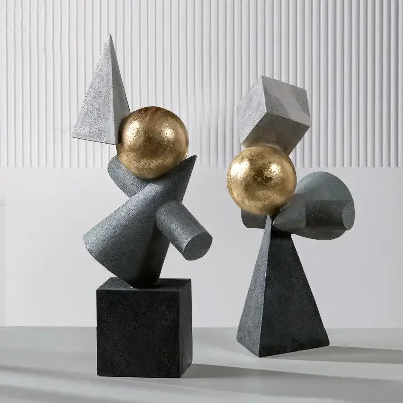 Two abstract gray resin sculptures with geometric gold ball accents on black bases for decorbites geometric gold decor