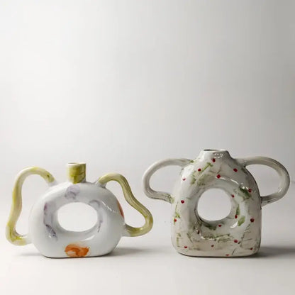 Two ceramic vases with abstract handle ceramic design and hand-painted floral accents in muted green and red decorbites abstract handle