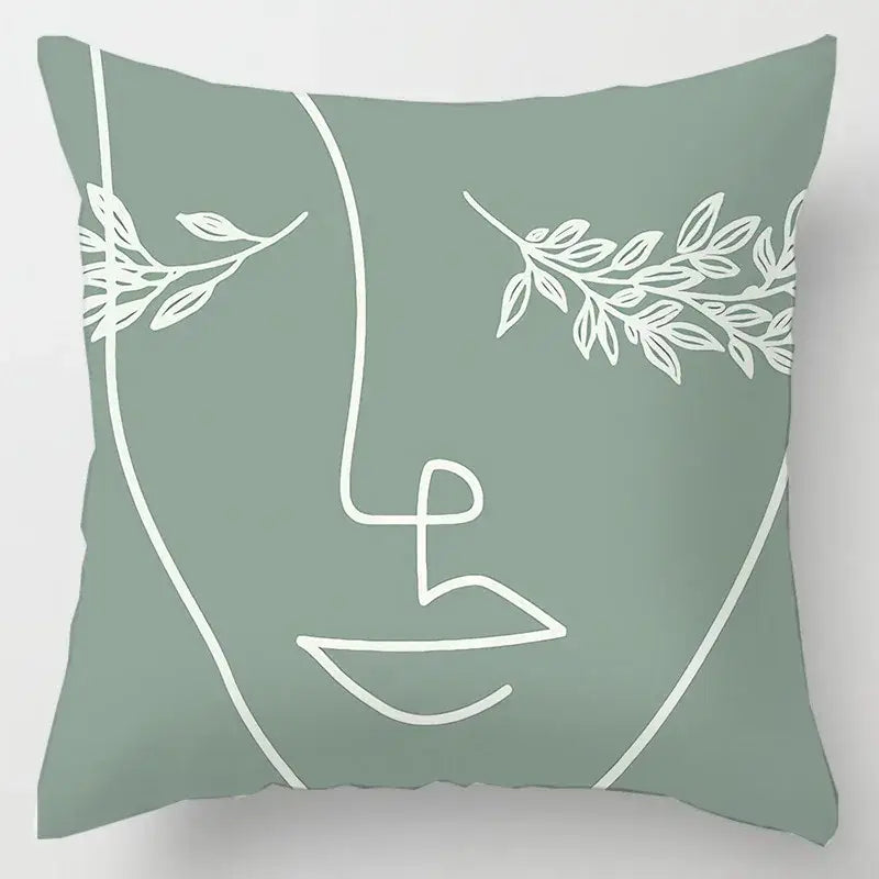 A sage green cushion cover with a minimalist white line-art abstract face and geometric leaves print