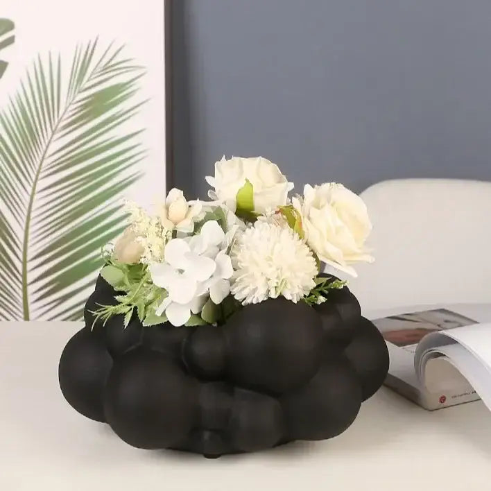 Black matte abstract patchwork ceramic vase with bubbly cloud design holding white artificial flowers for living room decor