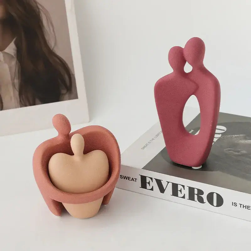 Two minimalist ceramic art couple statues in terracotta and dusty rose with heart-shaped and oval cutouts for decor