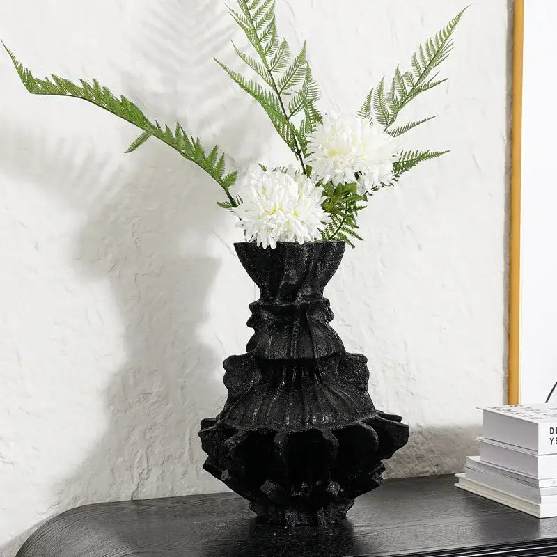 Black resin abstract pleated gear vase with ruffled corset design holding white flowers and green ferns for living room decor