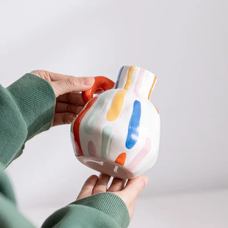 A white cartoon ceramic vase teapot with vibrant orange blue yellow pink stripes and a bold red handle for decorbites decor