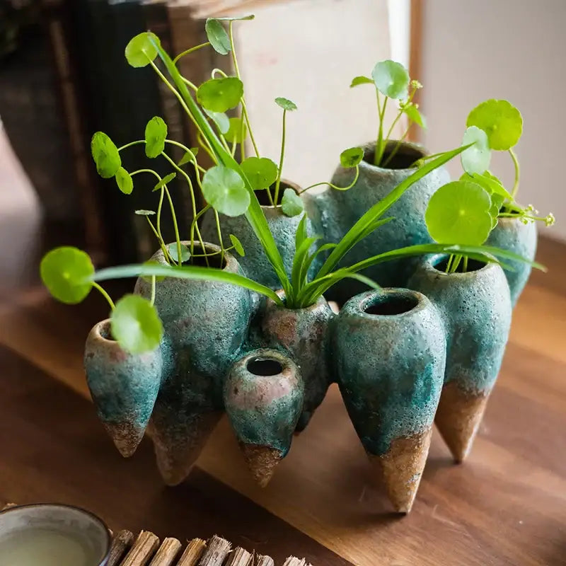 A cluster of teal ceramic hanging vases with brown bases holding green plants decorbites abstract tooth living room decor