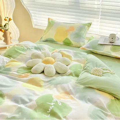 A plush white and yellow flower pillow on a bed with an abstract watercolor pastel green and yellow decorbites cute pattern duvet cover
