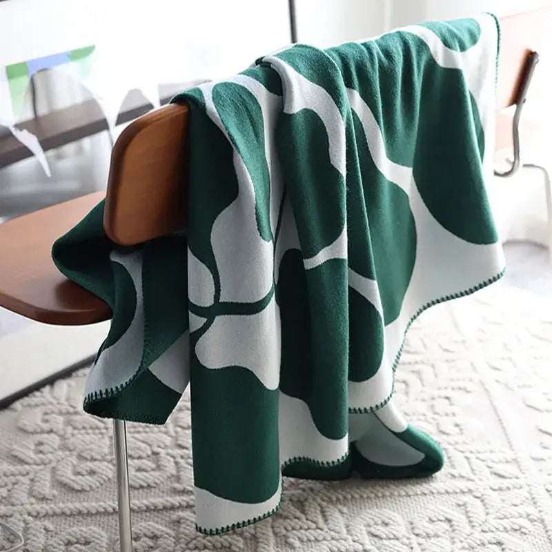 A plush green and white throw blanket with bold leaf pattern draped on a wooden chair featuring decorbites jacquard imitation cashmere
