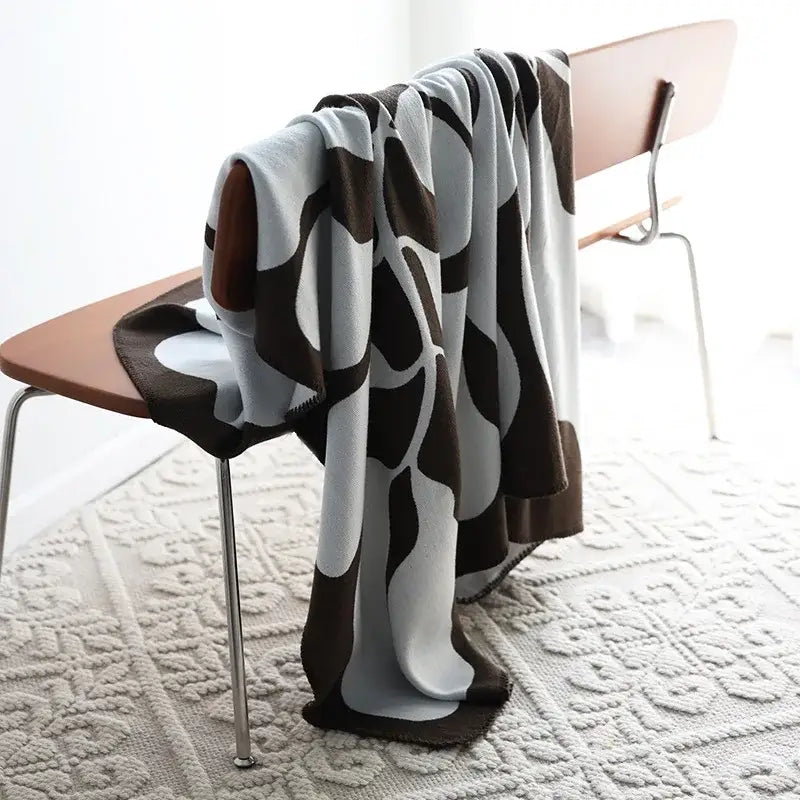 A soft brown and white abstract wavy jacquard imitation cashmere throw blanket draped over a wooden chair