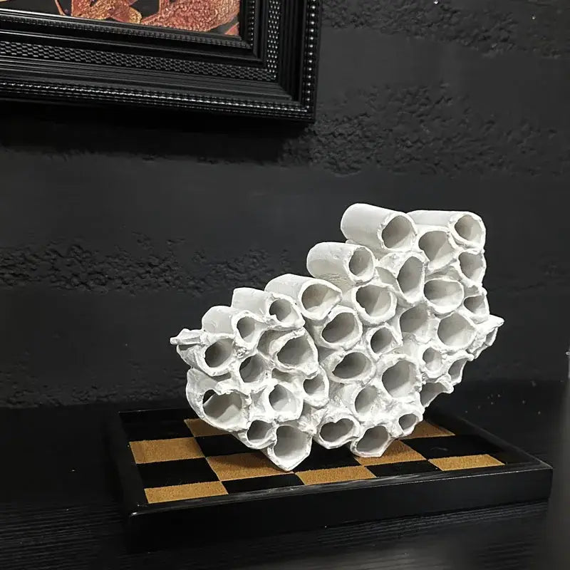 Abstract white ceramic honeycomb mesh conduit sculpture resembling interconnected tubes on black and gold base