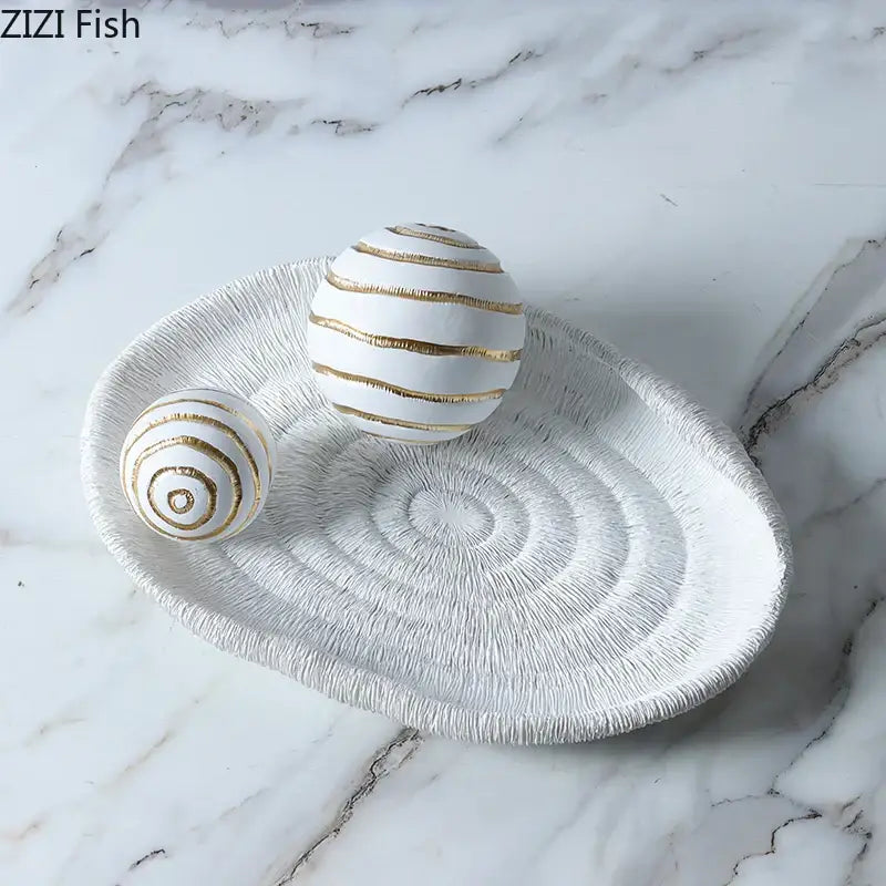 White ceramic tray with textured concentric circles and gold stripes holding two golden texture ball sculptures for living room decor