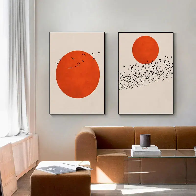 Two minimalist nordic style canvas prints with bold orange circles and black bird silhouettes on cream winter morning landscape background