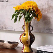 Glossy ceramic vase plant with vibrant yellow red and black abstract design and gold toned ring handles for living room decor