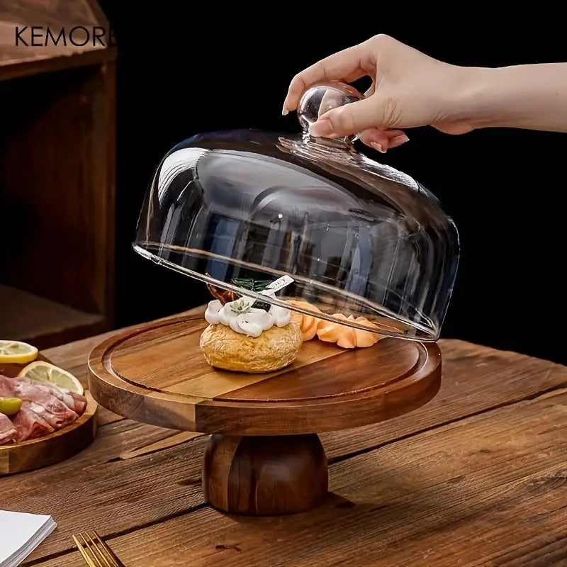 Acacia wood cake stand with a clear glass dome and rounded knob handle resting on dark wood for dessert display