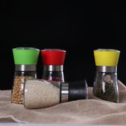Adjustable spice grinder set with colorful green red and yellow silicone tops and one black spice grinder on burlap surface