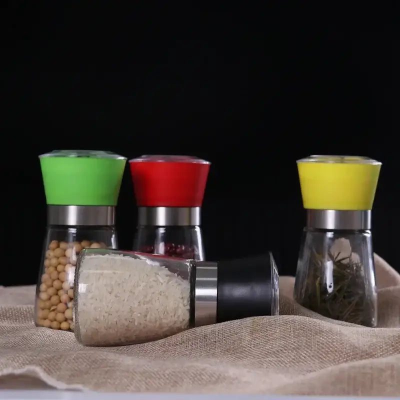 Adjustable spice grinder set with colorful green red and yellow silicone tops and one black spice grinder on burlap surface