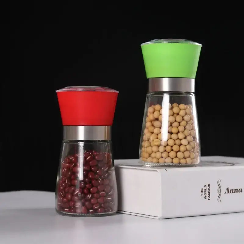Adjustable spice grinder set featuring red and green silicone tops with clear glass bodies and stainless steel bands