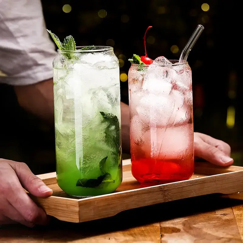 Two tall clear glass tumblers filled with ice garnished with mint and cherry from an aesthetic drinking glasses set
