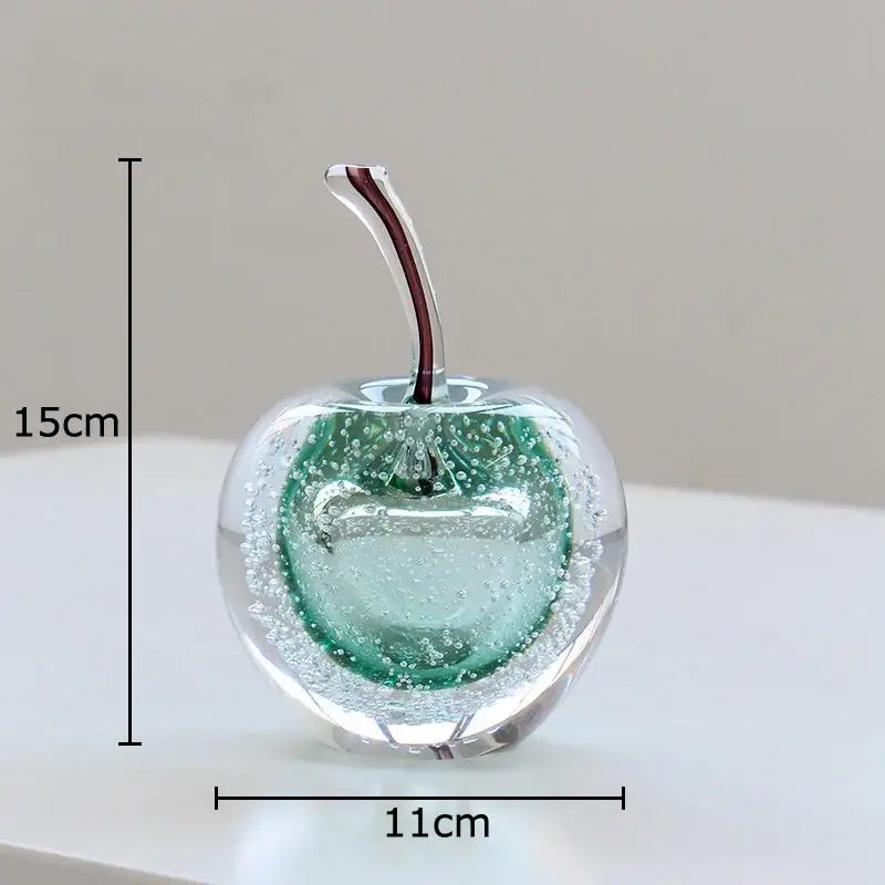 A translucent green and clear glass fruit sculpture desk ornament with a red stem and embedded bubbles