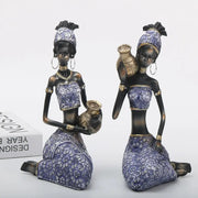 Two african woman sculptures dressed in purple and gold holding ceramic jugs for decorbites african woman decor
