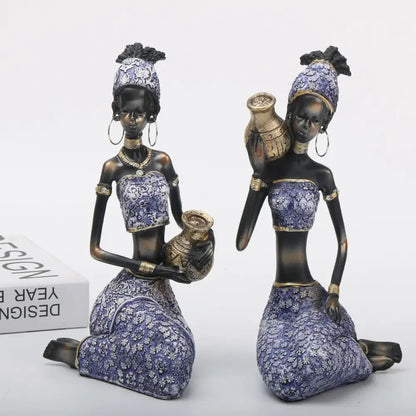 Two african woman sculptures dressed in purple and gold holding ceramic jugs for decorbites african woman decor