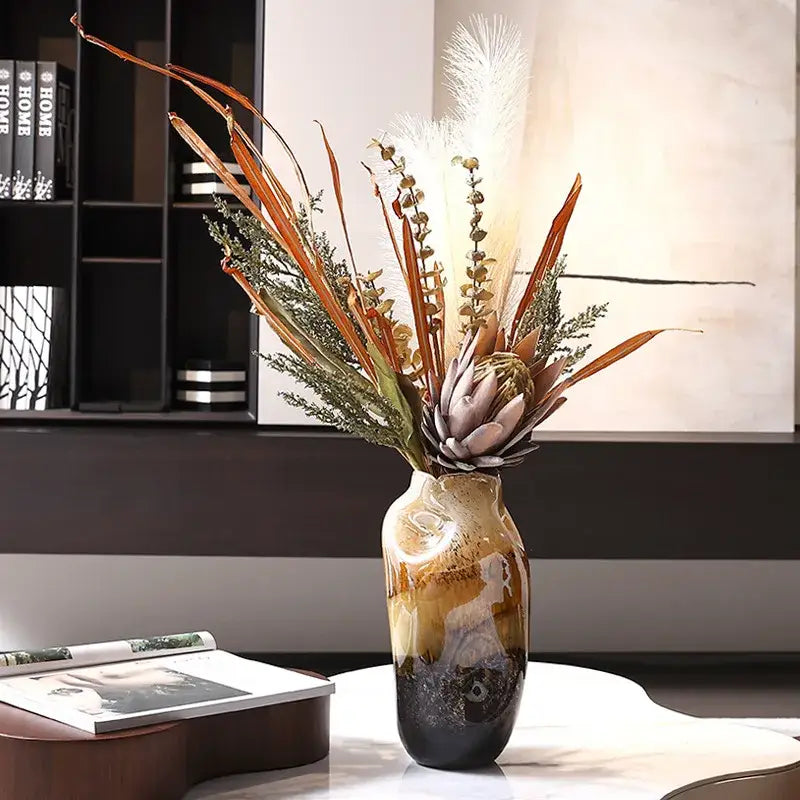 A tall glossy ceramic gradient glass vase in amber and dark brown hues with an irregular floral arrangement