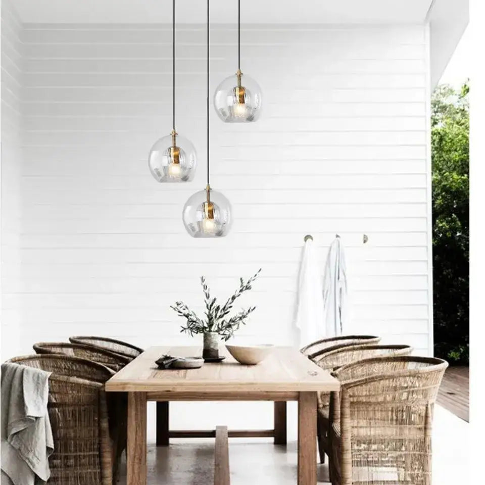 Three clear glass pendant lights with brass accents hang above a wooden dining table in kitchen gold globe cord style