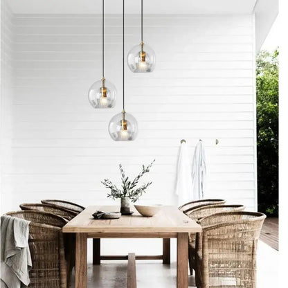 Three clear glass pendant lights with brass accents hang above a wooden dining table in kitchen gold globe cord style