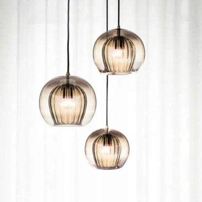 Three spherical amber glass pendant lights with vertical ribbed texture and black cords for kitchen lighting