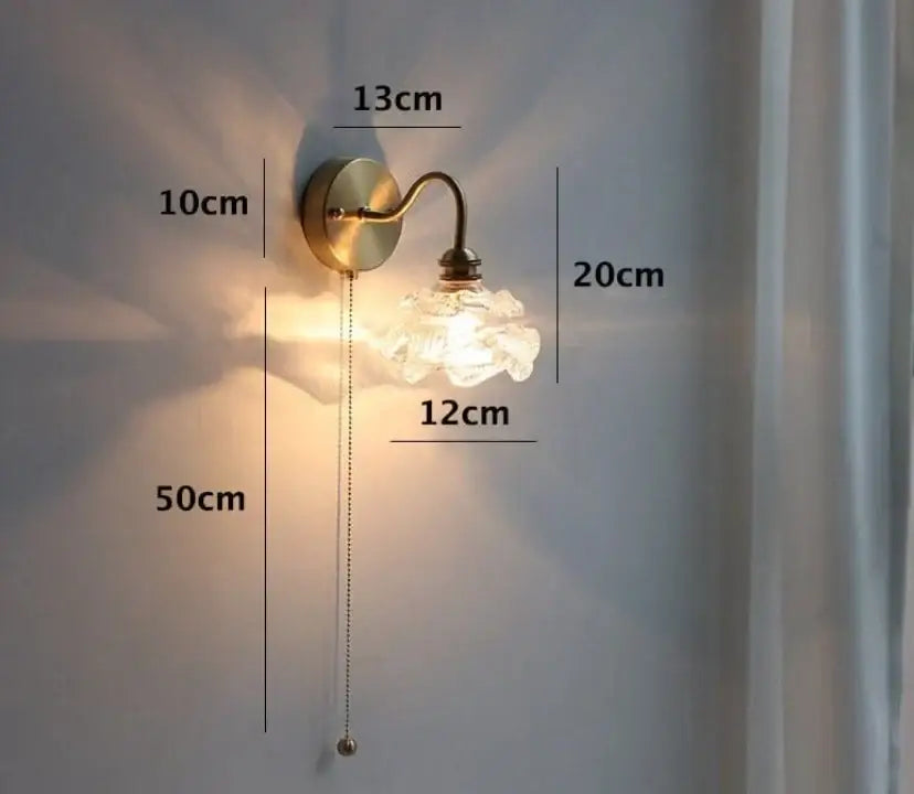 A vintage-style brass wall sconce with a frosted glass flower shade complements amber and cream glass pendant light designs
