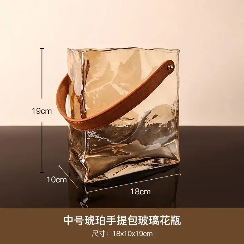 Translucent amber bag shape glass vase with hammered finish and brown leather handle for living room decor