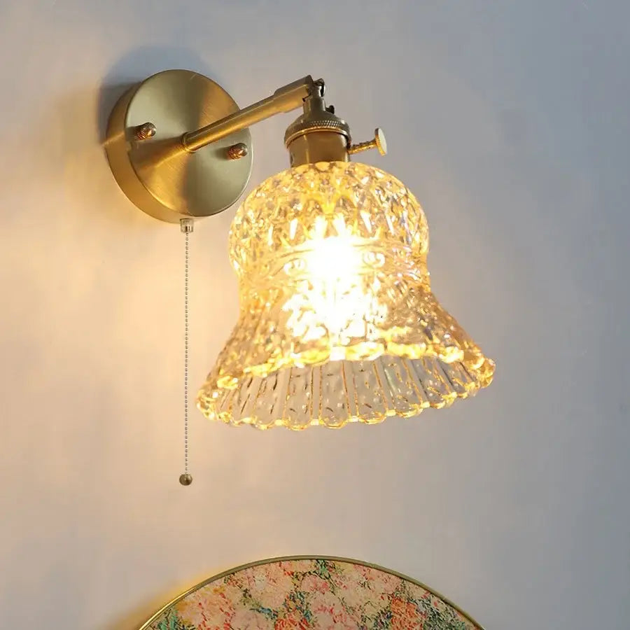 Vintage-style brass wall light fixture with faceted bell-shaped amber flower crystal glass shade and pull chain for bedroom