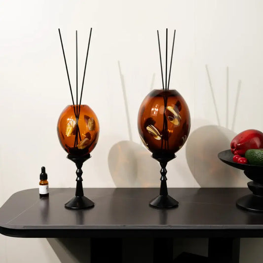 Two amber geometric circle glass reed diffusers with golden leaf accents and black metal stands for living room decor