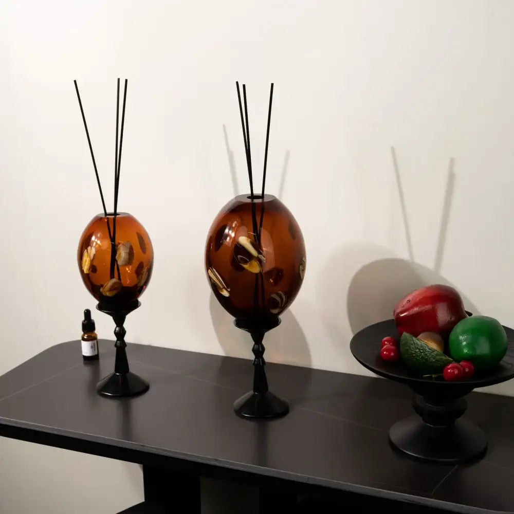 Two amber geometric circle glass reed diffusers with black metal stands and wooden decorbites reeds for living room decor