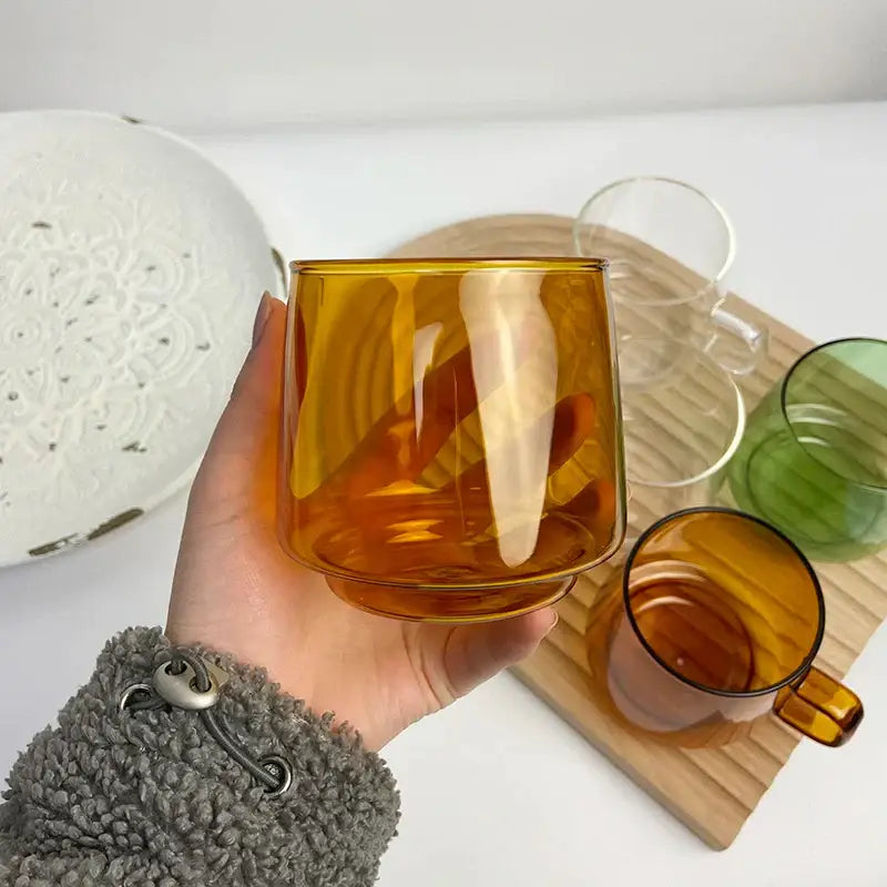 A hand holds a translucent amber glass coffee mug with a sturdy curved handle from decorbites glass coffee collection