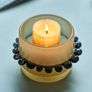 A translucent amber glass cylinder vase with black beaded rim holds a lit orange candle for living room decor