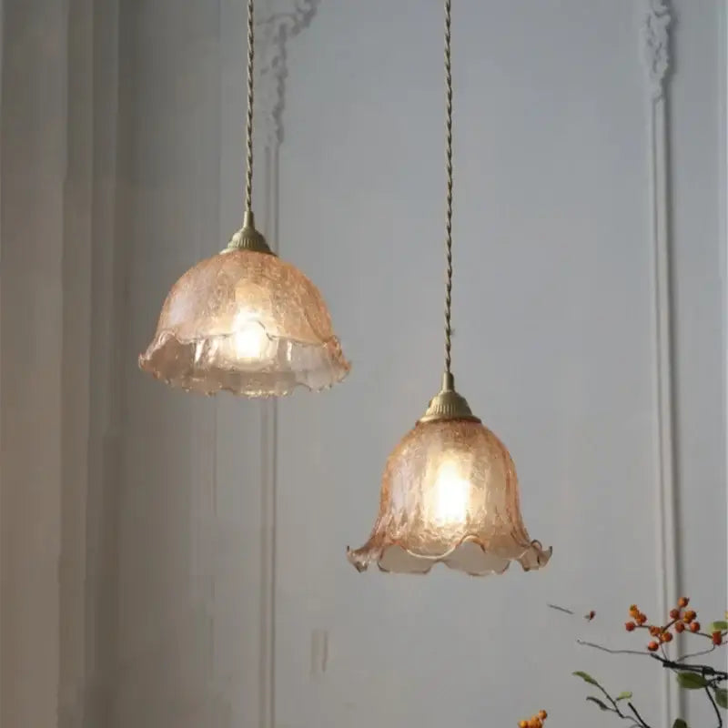 Two peach-colored amber glass led pendant lamps with ruffled edges and brass fixtures hang from twisted cords
