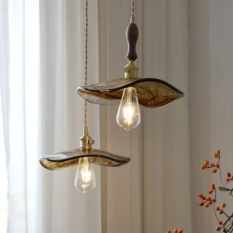 Two amber glass pendant lights with brass knob switch and wooden handles hang from ceiling for dining room decorbites brass knob