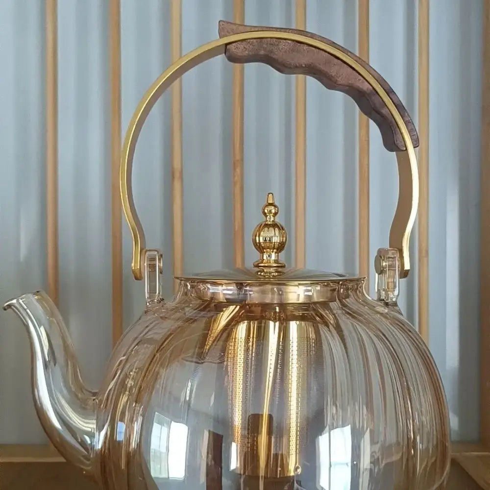Transparent amber glass teapot with gold-toned infuser lid and dark wooden handle grip from decorbites amber glass collection
