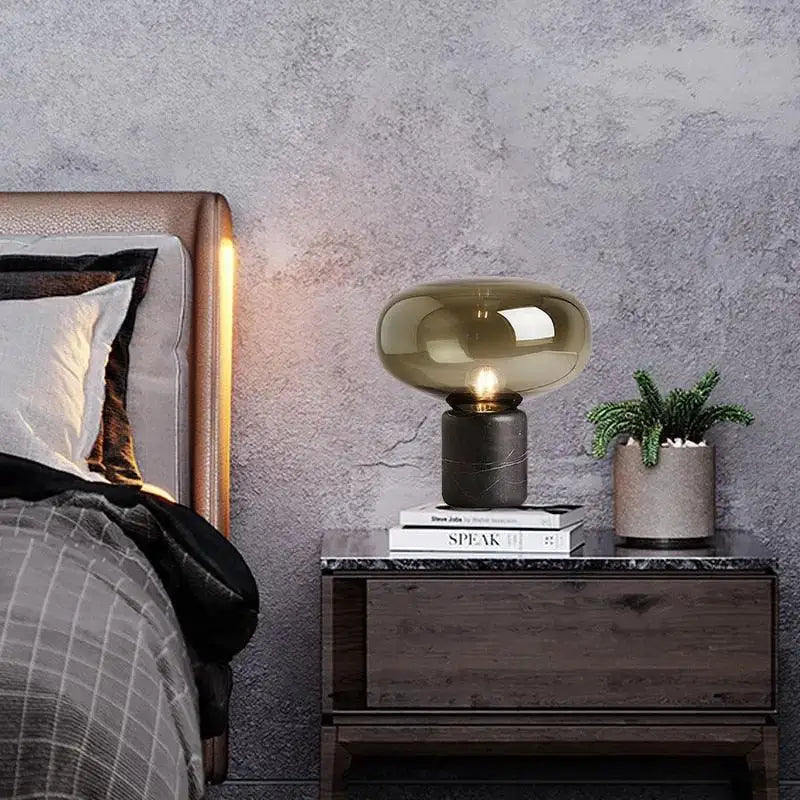 A nordic table lamp with a translucent amber glass dome and dark marble base for modern interior lighting