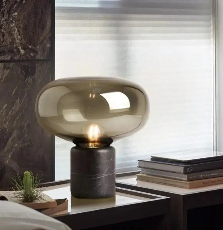 A sleek amber nordic table lamp with a translucent glass dome and dark gray marble base for modern interiors