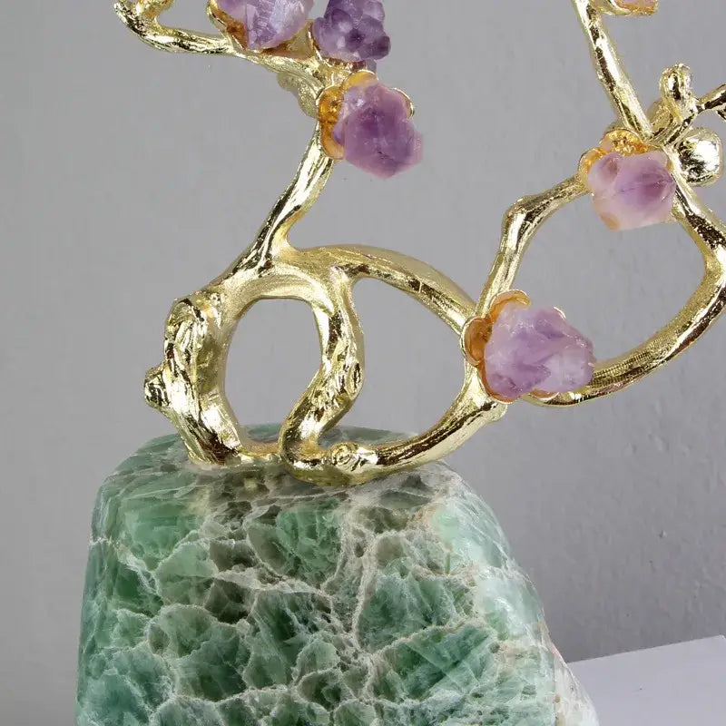 A golden brass tree ornament with raw amethyst crystals on a green and white veined aventurine base