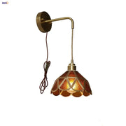 Antique brass wall light with warm amber glass led shade featuring geometric triangular patterns and scalloped edges