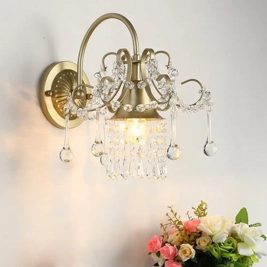 Antique brass wall light sconce with crystal teardrop accents and intricate filigree detailing for bedroom use