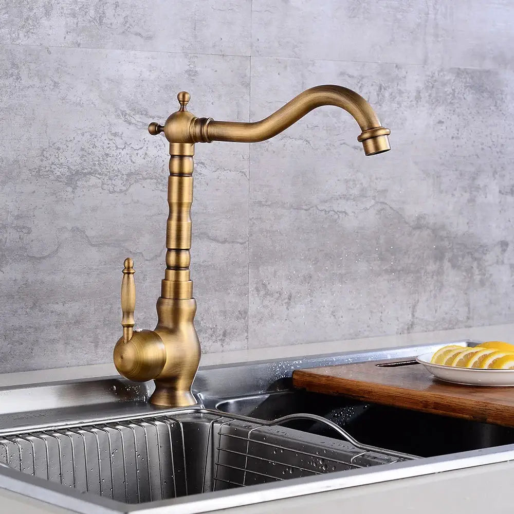 Antique brass and white ceramic kitchen faucet with a tall ornate spout and decorative handle swivel mixer