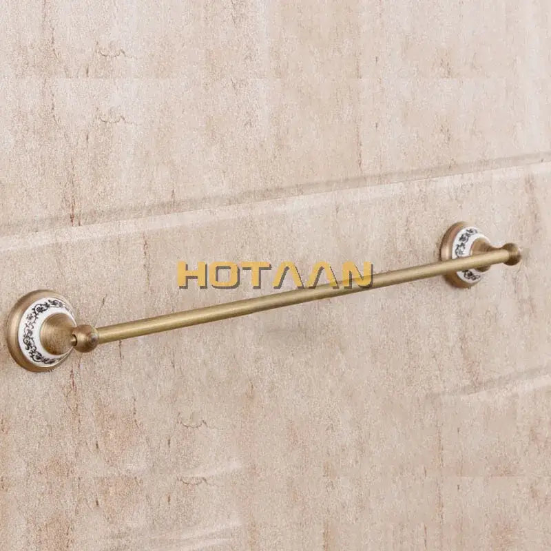 Antique brass towel rack with decorative ceramic end caps featuring black floral patterns in a brass bathroom accessories set