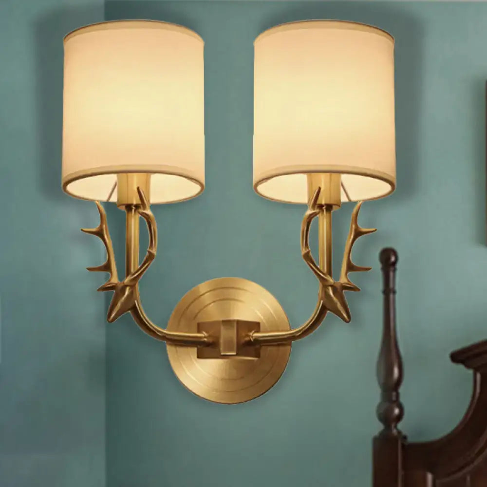 Antique brass antler wall sconce with gold-toned arms and cream fabric shade in a stylish design for bedroom lighting