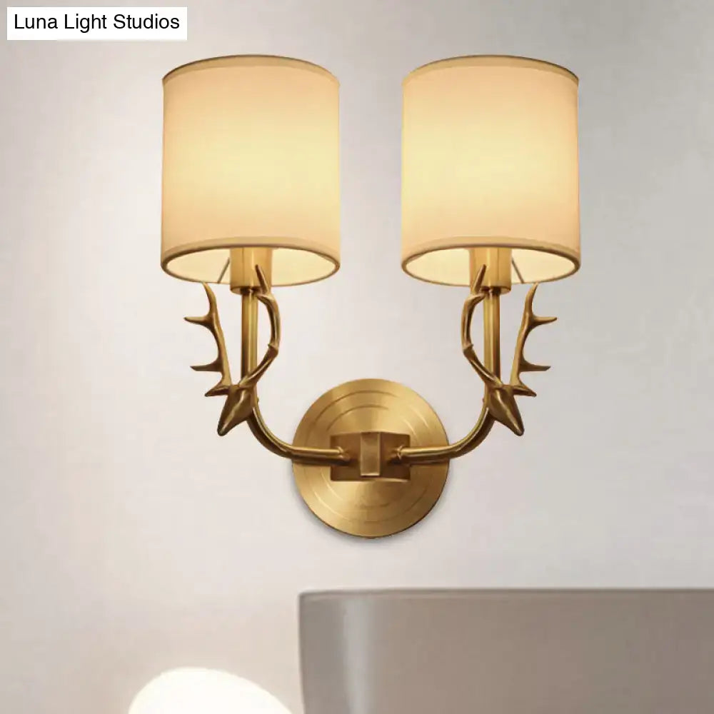 Antique brass antler wall sconce with fabric shade featuring brass finish and beige cylindrical shades for stylish bedroom lighting