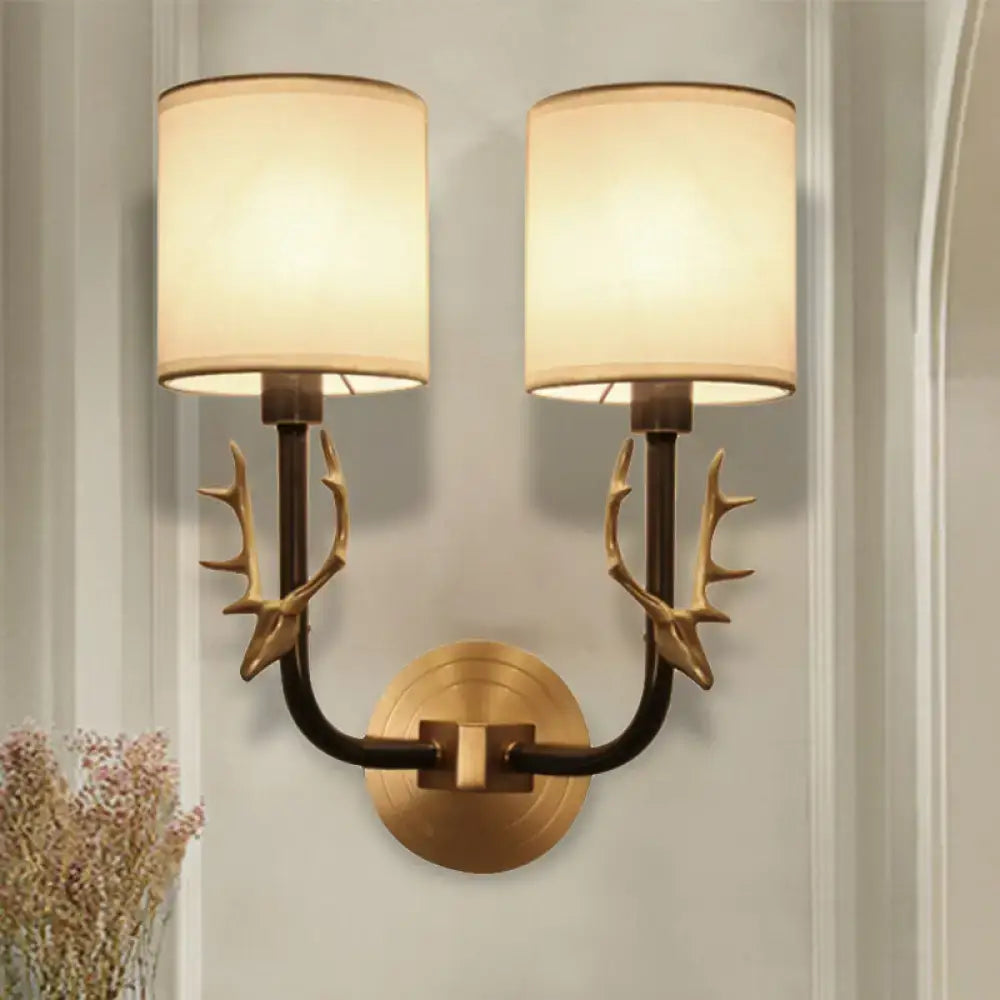 Antique brass antler wall sconce featuring stylish design with brass-toned arms and two cylindrical cream fabric shades for bedroom lighting