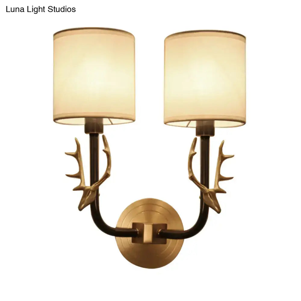 Antique brass wall sconce with deer antler arms and cream fabric shades for stylish bedroom lighting design