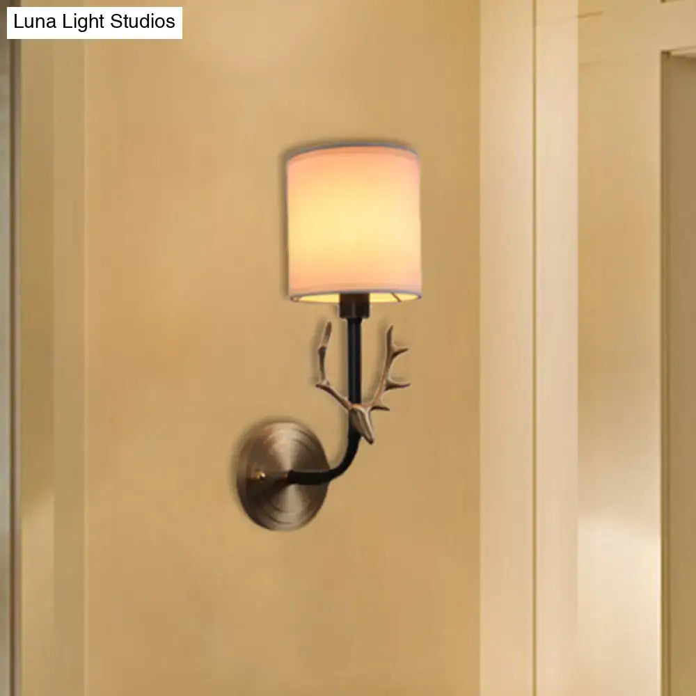 Antique brass antler wall sconce with matte black metal frame and off-white fabric shade for stylish bedroom lighting