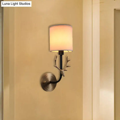 Antique brass antler wall sconce with matte black metal frame and off-white fabric shade for stylish bedroom lighting